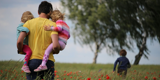 Male parent holding his children in his arms through the field 