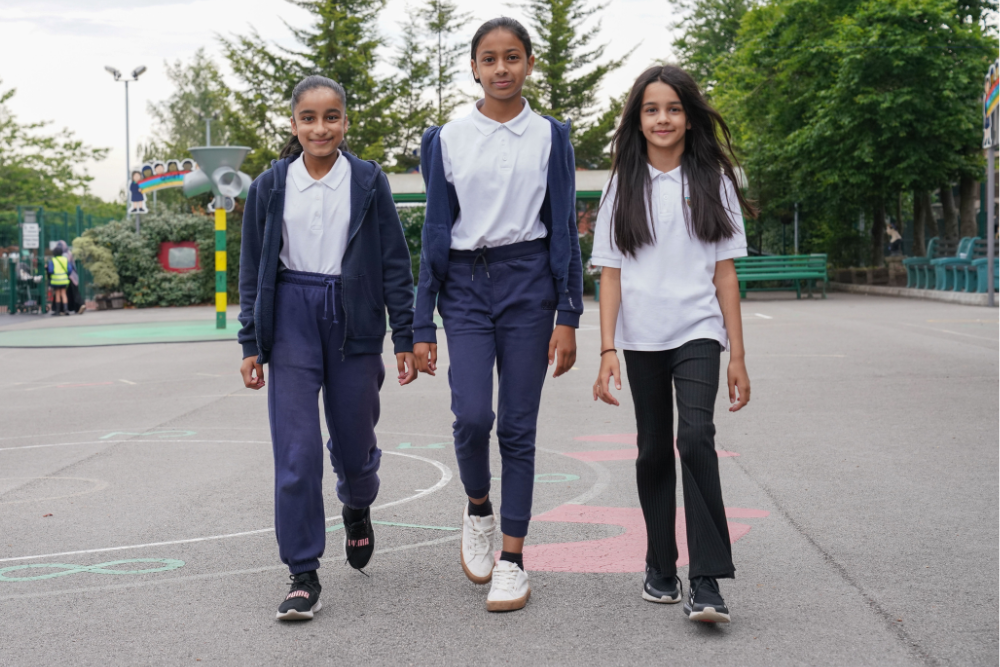 Three schoolchildren walk across their scjhool playground