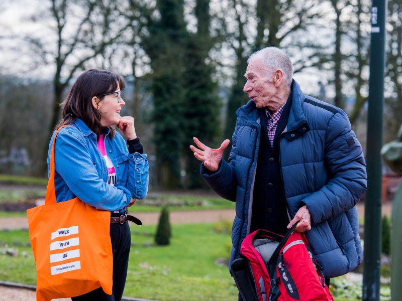 two people chatting a park one is wearing a living streets bag