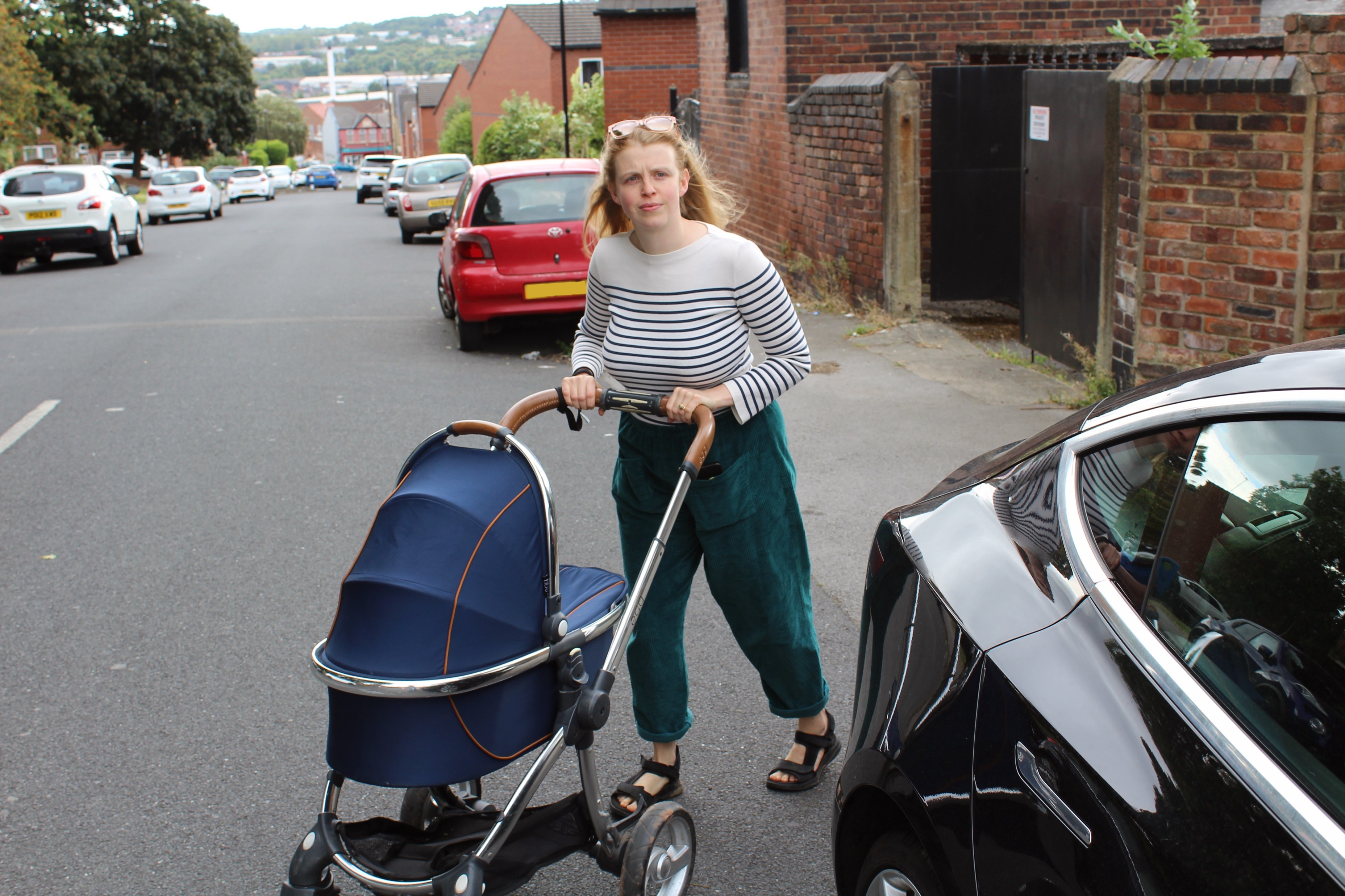 A parent moves out into the road with their pram to pass a car parked on the pavement